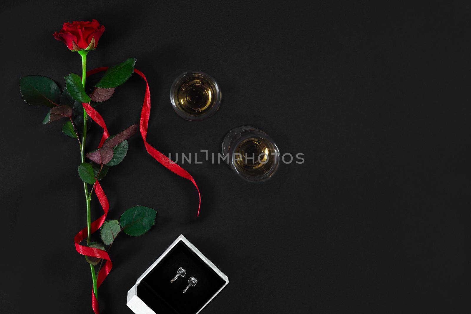 One dark red rose with red ribbon and box with earrings on black background. Romantic Valentines holidays concept. Valentine's day greeting card. Top view. Copy space. Still life. Flat lay