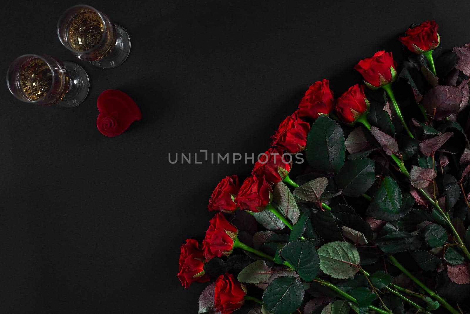 A bouquet of red roses and a box of ring on black background. View top. Flat lay. Copy space. Still life