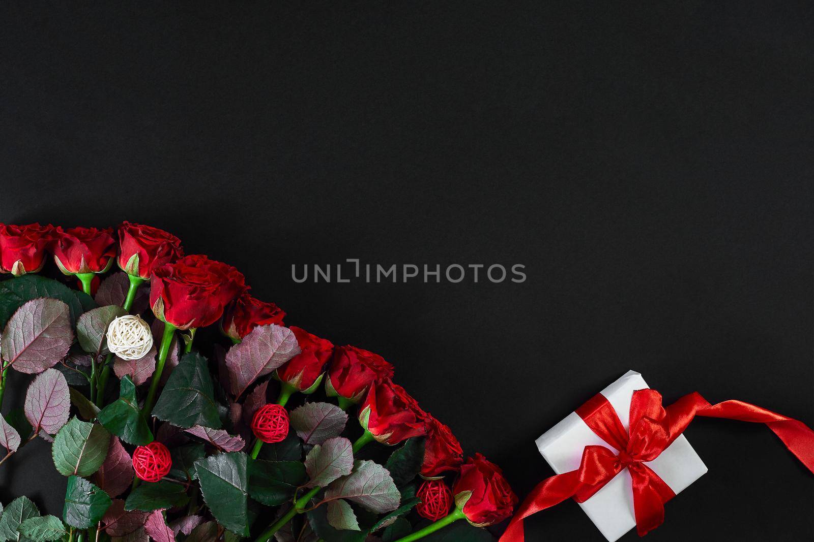 Red roses and white gift box with red ribbon on black background. Top view. Flat lay. Copy space. Still life