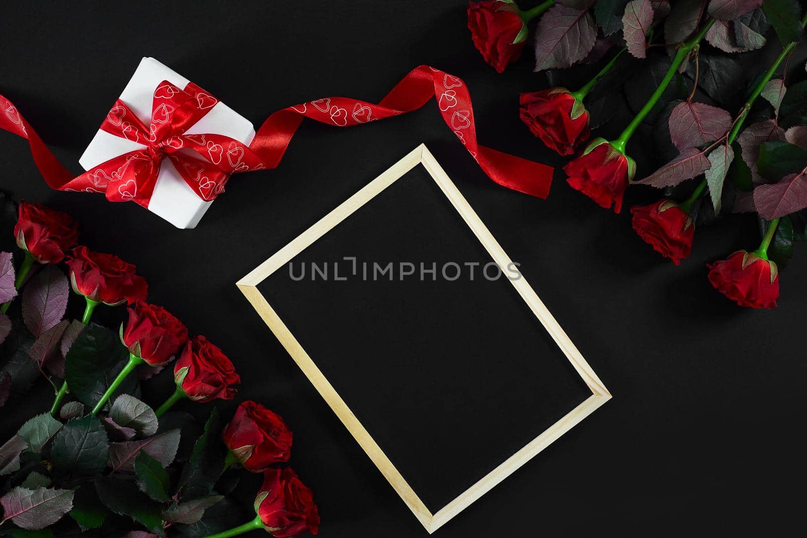 Red roses and empty chalk board on black background. Valentines day greeting card. Top view. Copy space. Still life. Flat lay