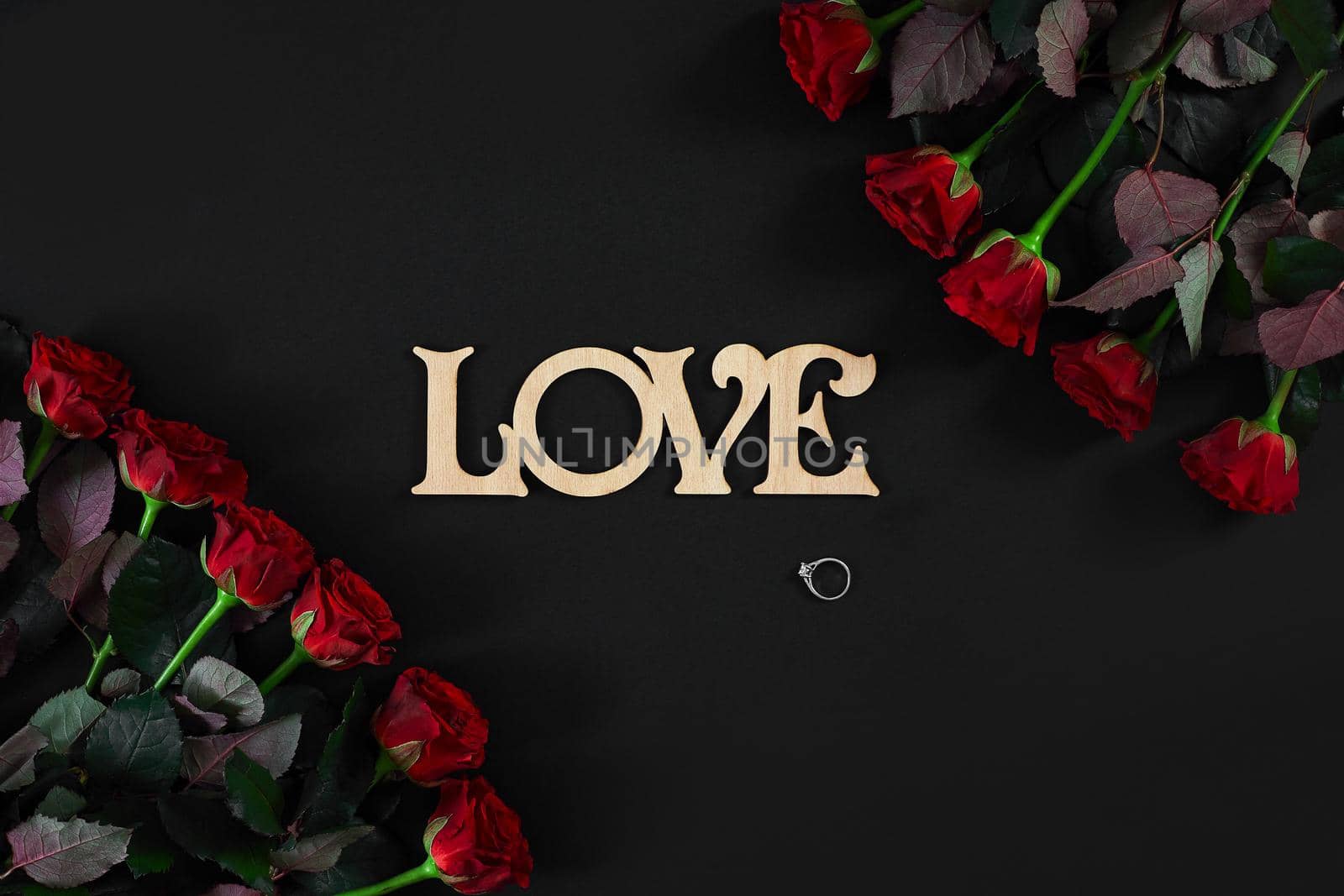 Red roses flowers with wooden word LOVE on black background with place for text. Romantic Valentines holidays concept. Valentine's day greeting card.. Copy space. Still life. Flat lay