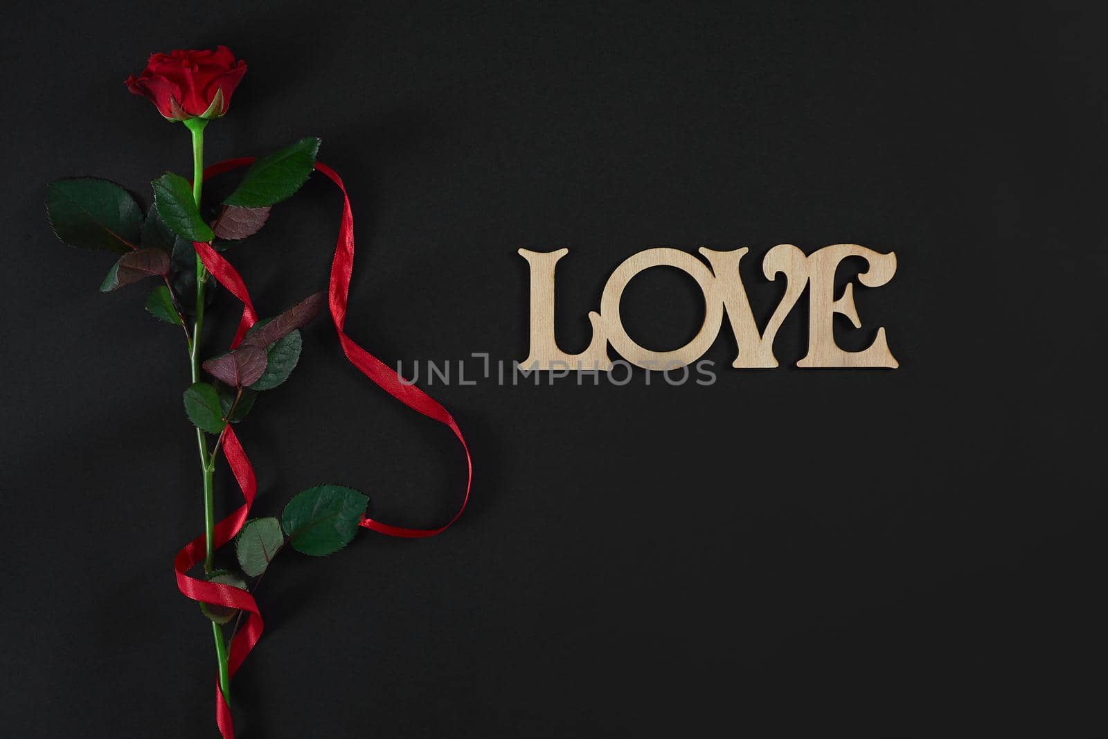 One dark red rose with red ribbon on black background. Romantic Valentines holidays concept. Valentine's day greeting card. Top view. Copy space. Still life. Flat lay