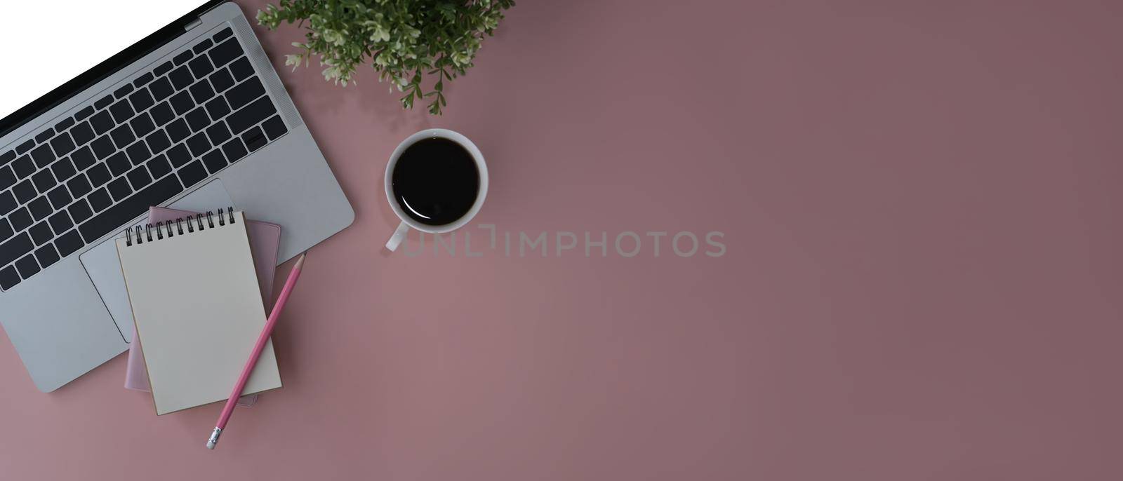 Flat lay laptop computer, coffee cup, notebook and potted plant on pink background. Copy space.