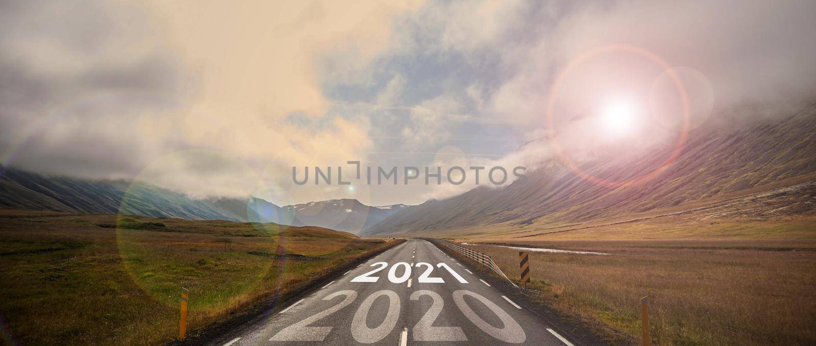 The word 2021 written on highway road in the middle of empty asphalt road at golden sunset and beautiful blue sky. by driver-s