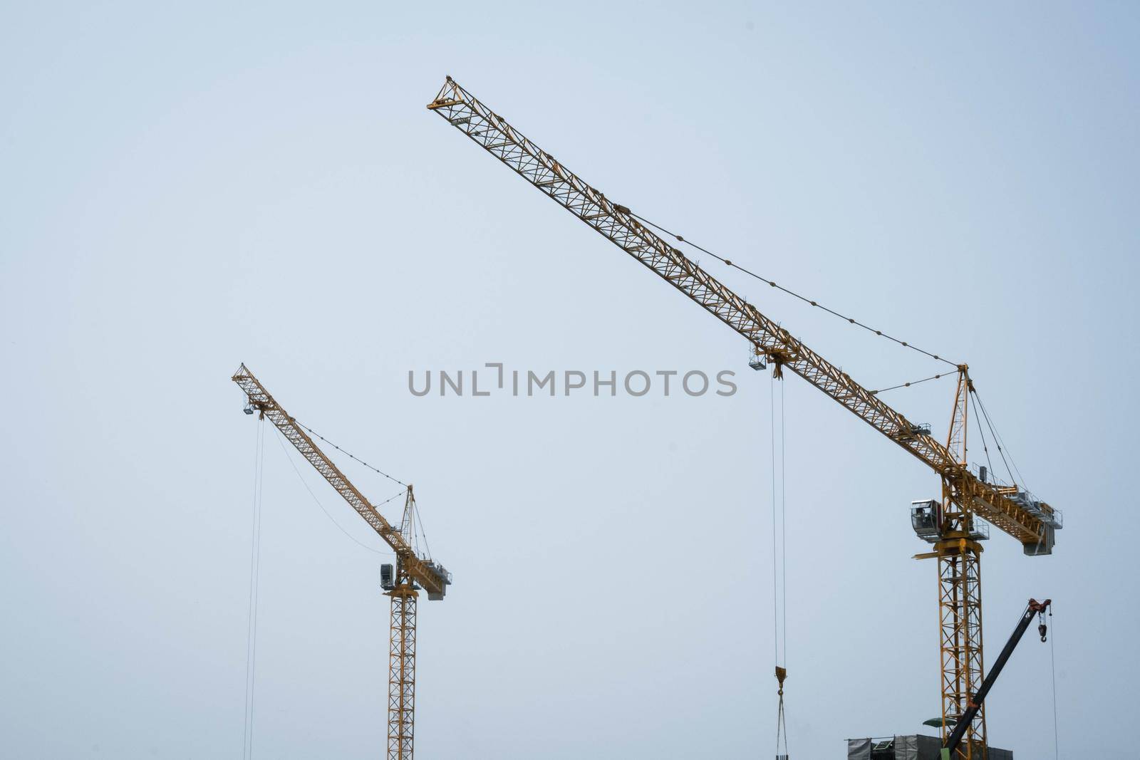 Tower cranes working on a construction site lifts a load at high-rise building in summer day. A large construction site with busy cranes. by TEERASAK