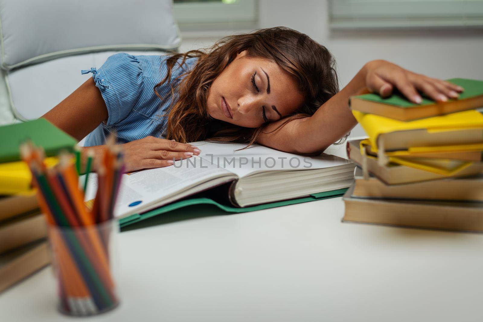 A beautiful tired young female student is sleeping on the books while preparing exam and learning lessons in school library.