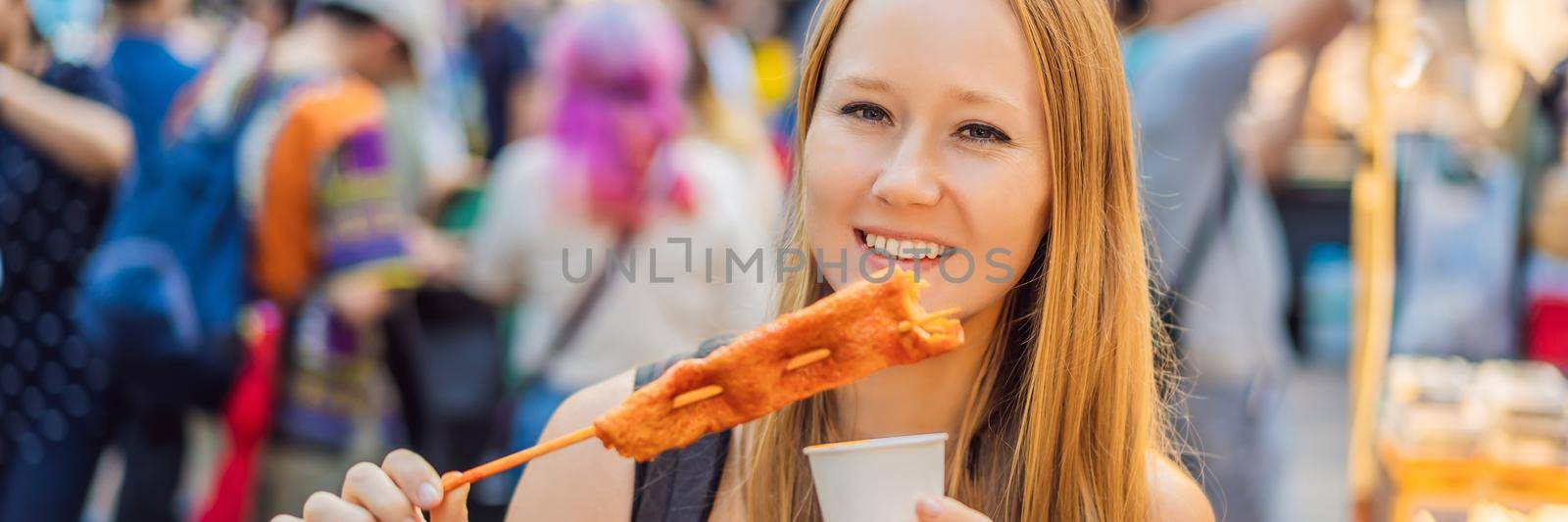 Young woman tourist eating Typical Korean street food on a walking street of Seoul. Spicy fast food simply found at local Korean martket, Soul Korea. BANNER, LONG FORMAT
