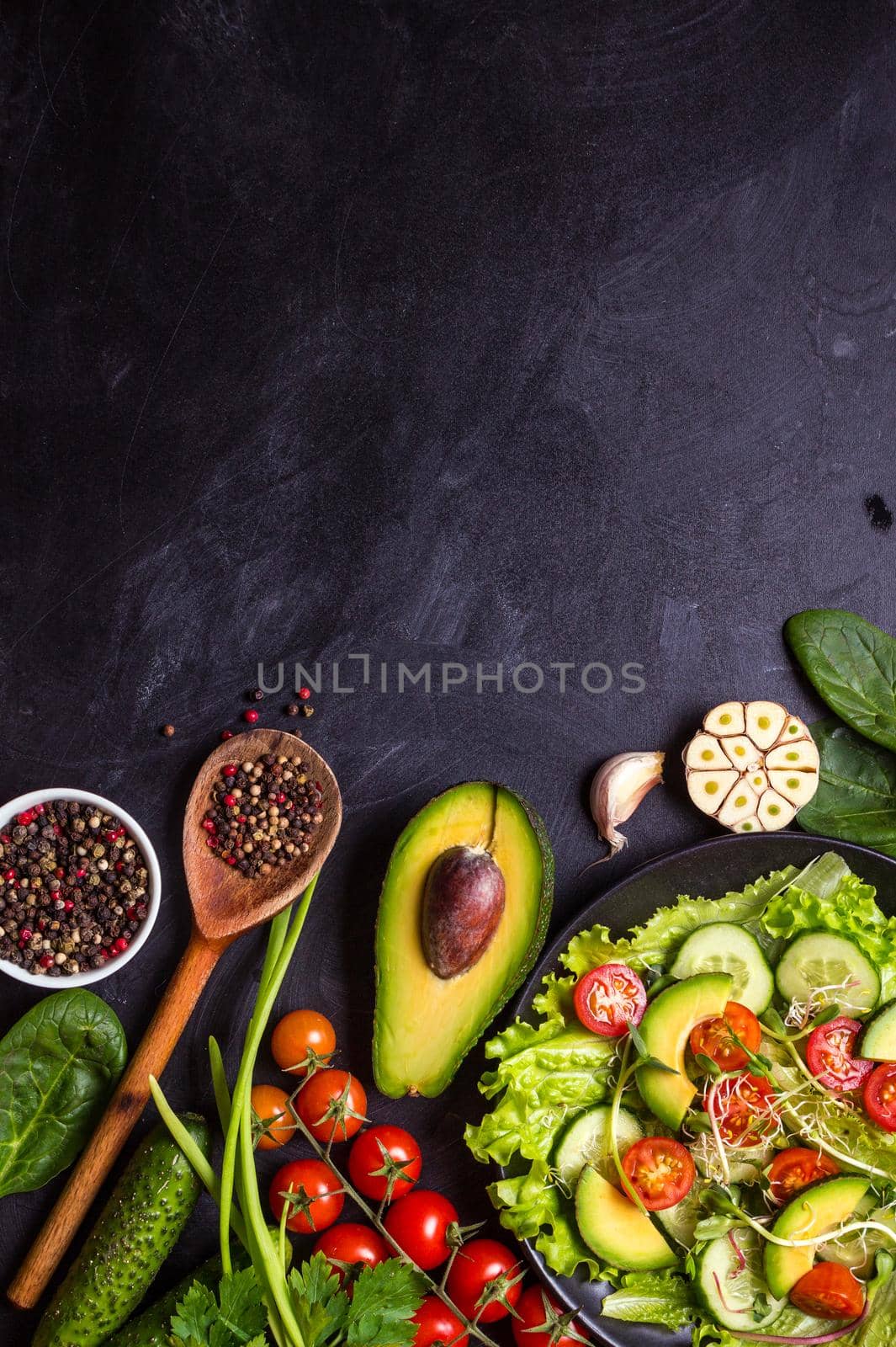 Ingredients for making salad on rustic black chalk board background. Vegetable salad in bowl, avocado, tomato, cucumber, spinach. Healthy, clean eating concept. Vegan or gluten free diet. Copy space