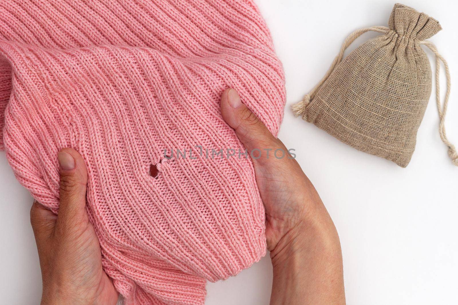 Top view of cropped woman hands holding pink wool fabric with hole made by moth and bag with dry herb on white background