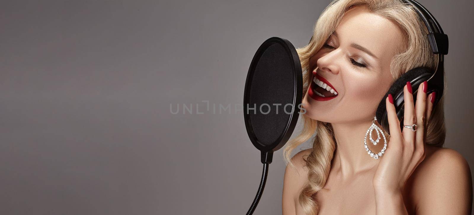 Beautiful Blonde Woman Singing Song in Professional Recording Studio with Microphone, Pop Filter and Headphones. Glamour Pop Diva Creates New Musical Track. Music Karaoke with Female Vocal Artist.