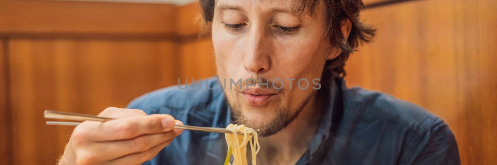 Male tourist eating Korean noodles in a Korean cafe. Travel Korea Concept BANNER, LONG FORMAT by galitskaya