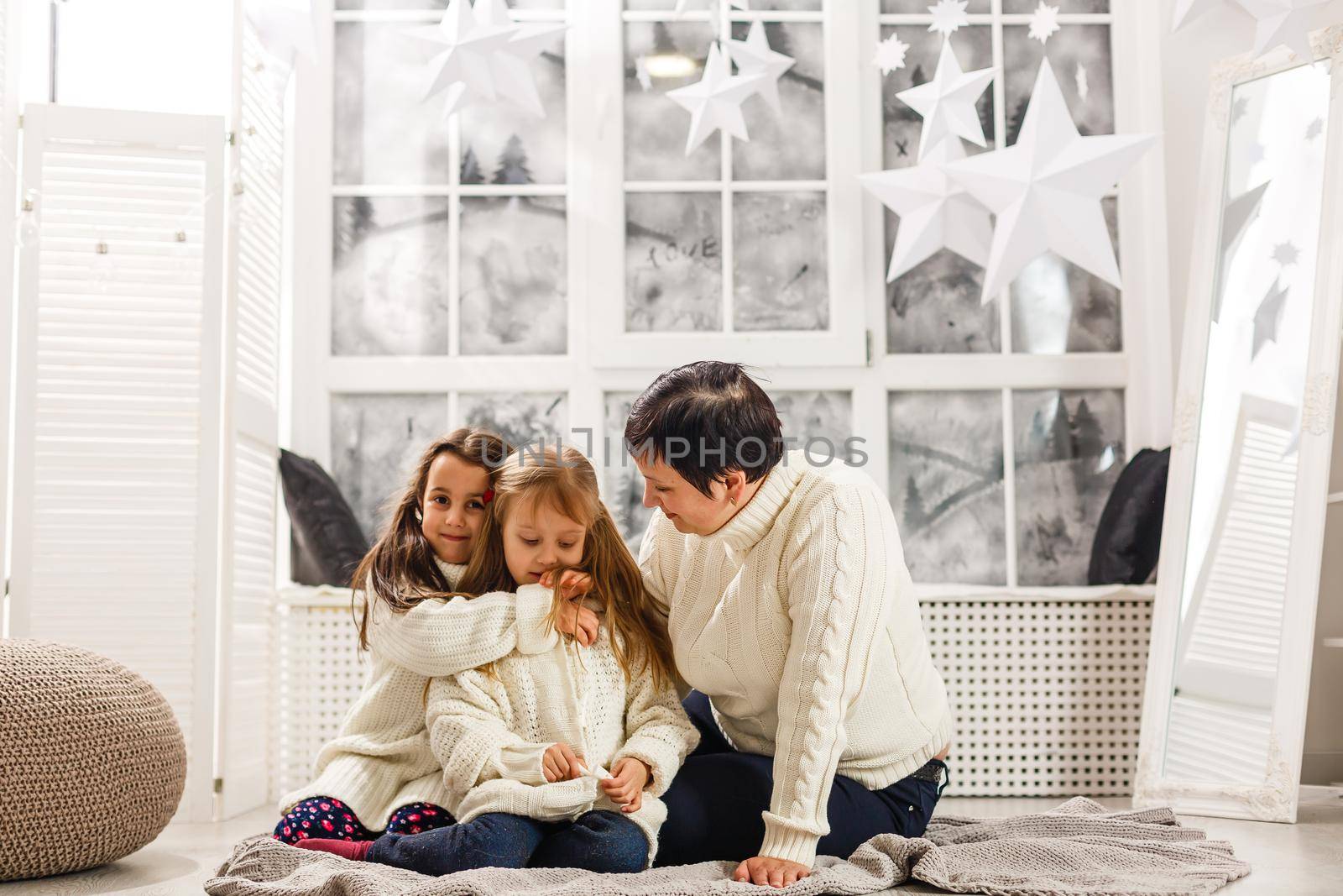 Merry Christmas and Happy Holidays. Cheerful mom and her cute daughters girls exchanging gifts. Parent and two little children having fun and playing together near Christmas tree indoors