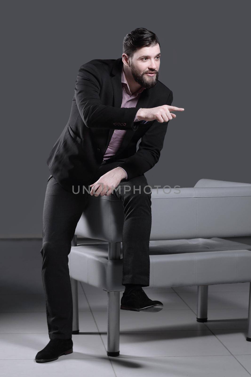 modern businessman sitting on the back of the chair and showing finger forward.