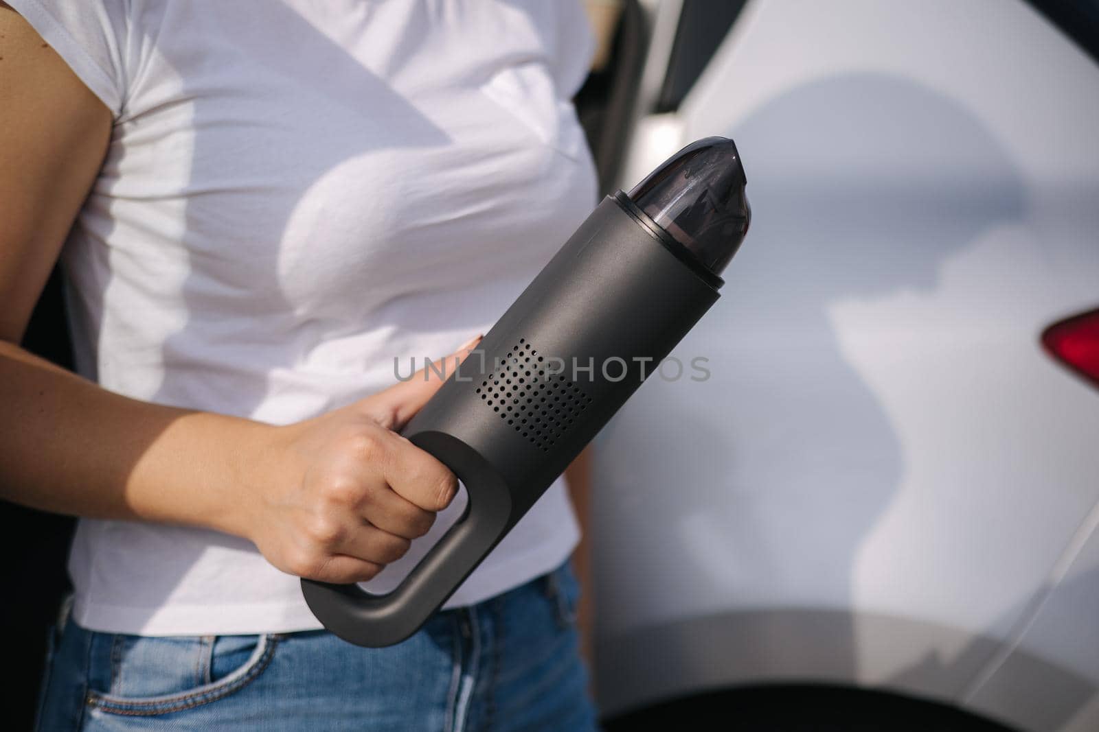 Woman hold portable vacuum cleaner in front of car. Attractive young woman prepare for cleaning in garage. Close-up of hands.
