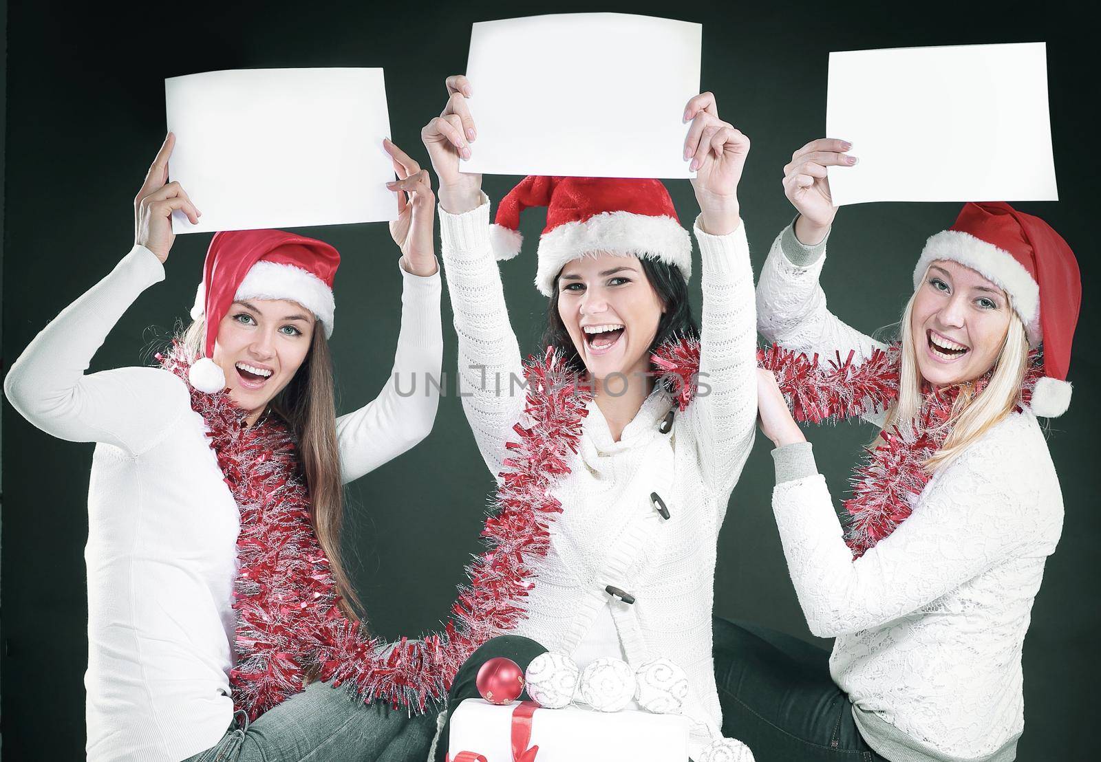 three young girls in costume of Santa Claus showing blank sheets. isolated on black