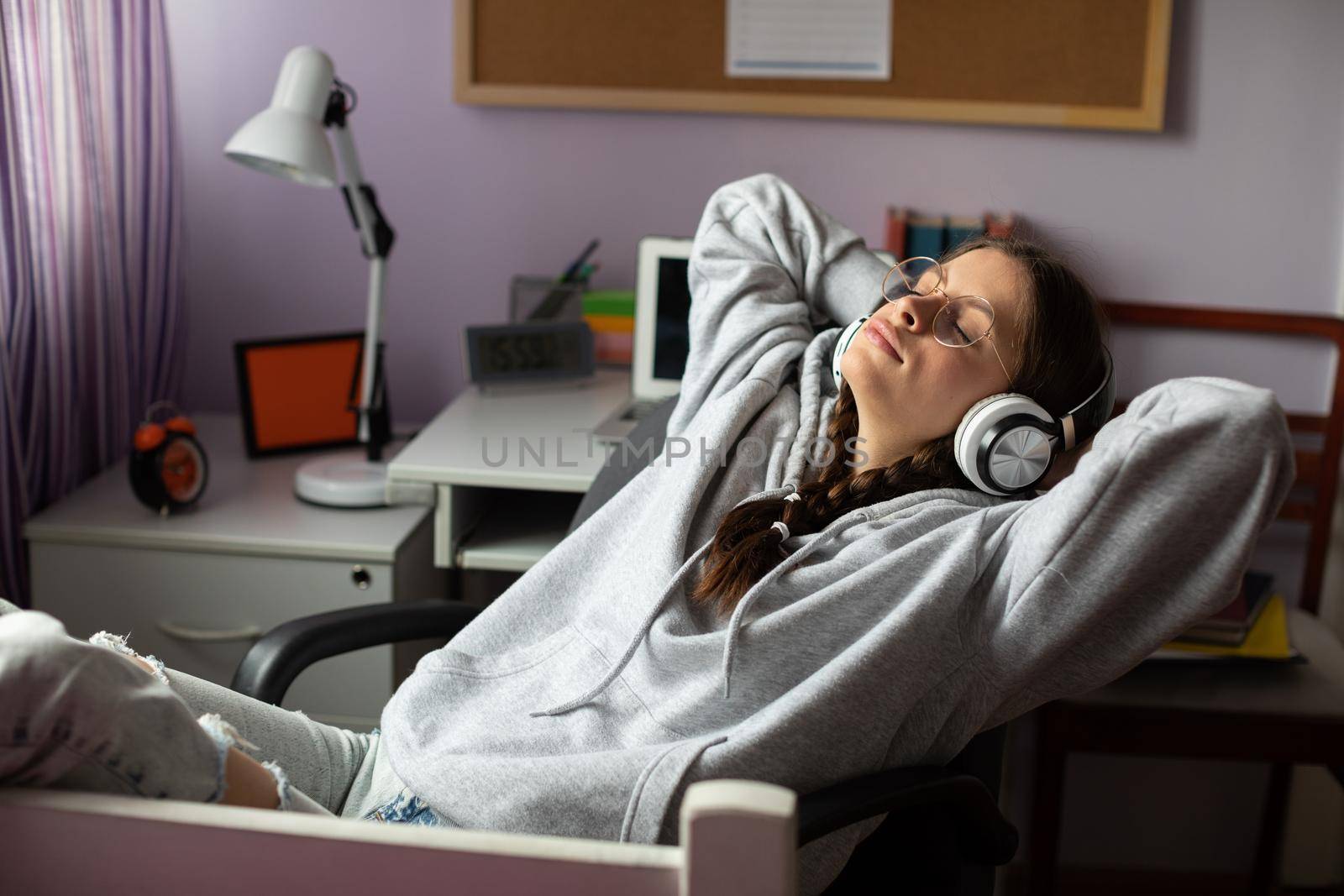 Hands above your head and eyes closed. Complete relaxation while listening to music. Young girl with pigtails and glasses is listening to music.