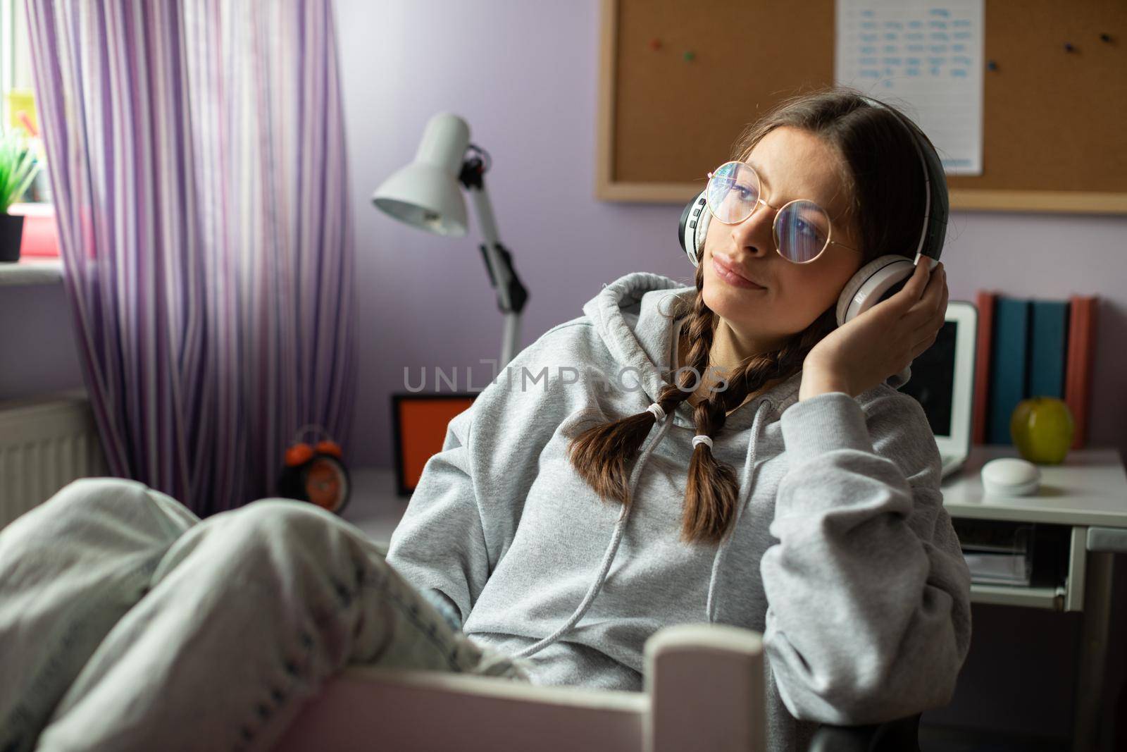 A teenage girl muses while listening to her favorite music. A young girl looks into the distance with headphones on her ears.