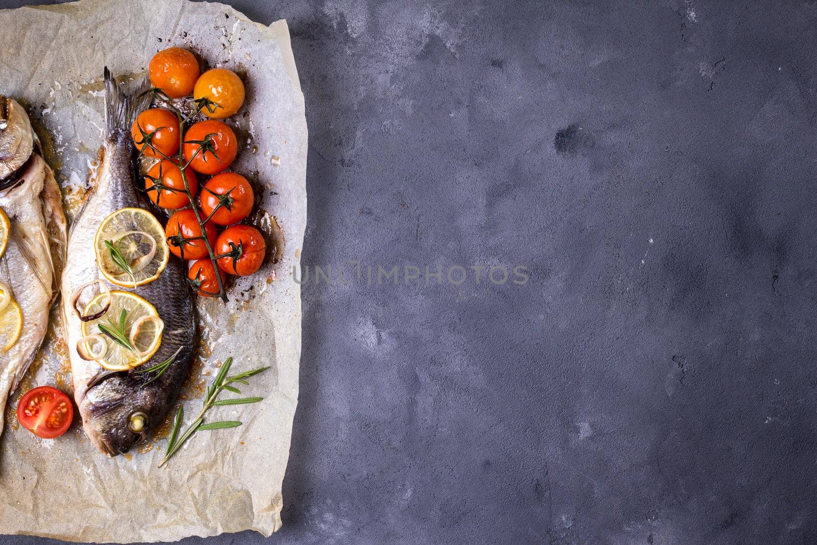 Tasty baked fish on dark rustic background. Baked sea bream with lemon, onion, herbs, tomatoes, spices. Space for text. Grilled delicious fish background. Diet and healthy food concept. Top view