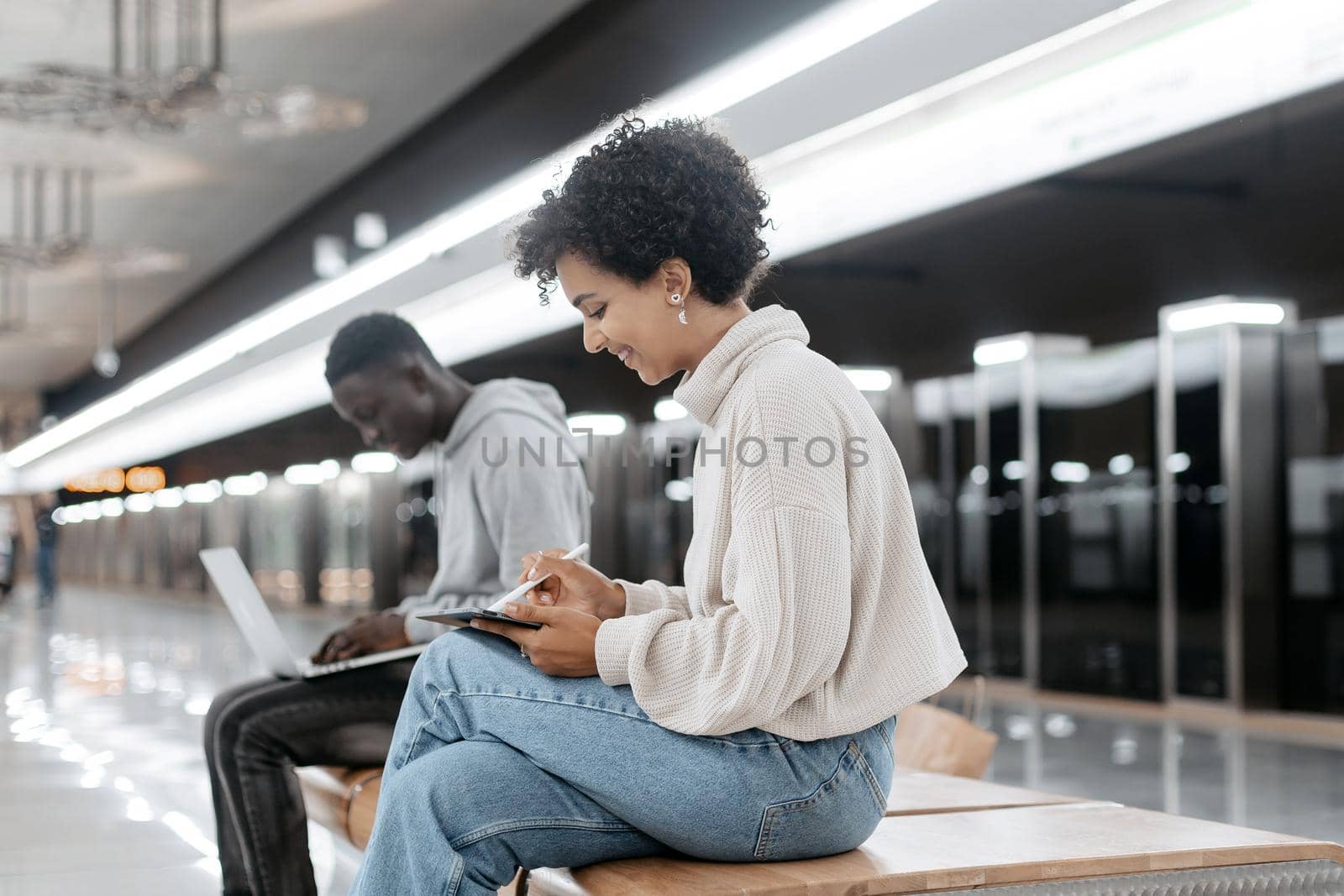 young people with their devices sitting on a bench in the subway . people and technology.