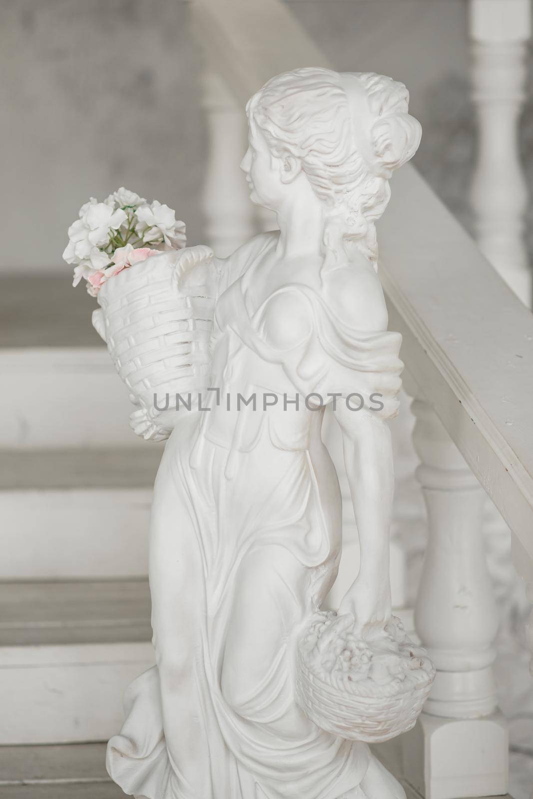 Sculpture of a girl with a basket of flowers standing by the stairs.
