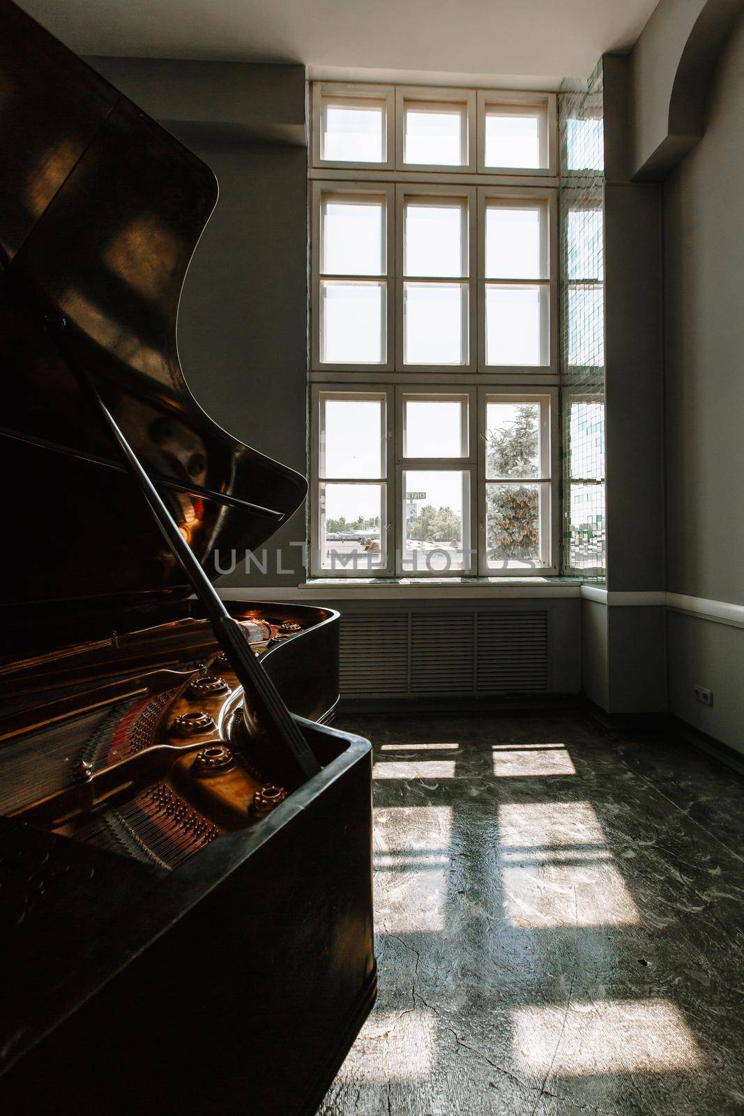 A black piano standing in a photo studio. Open window