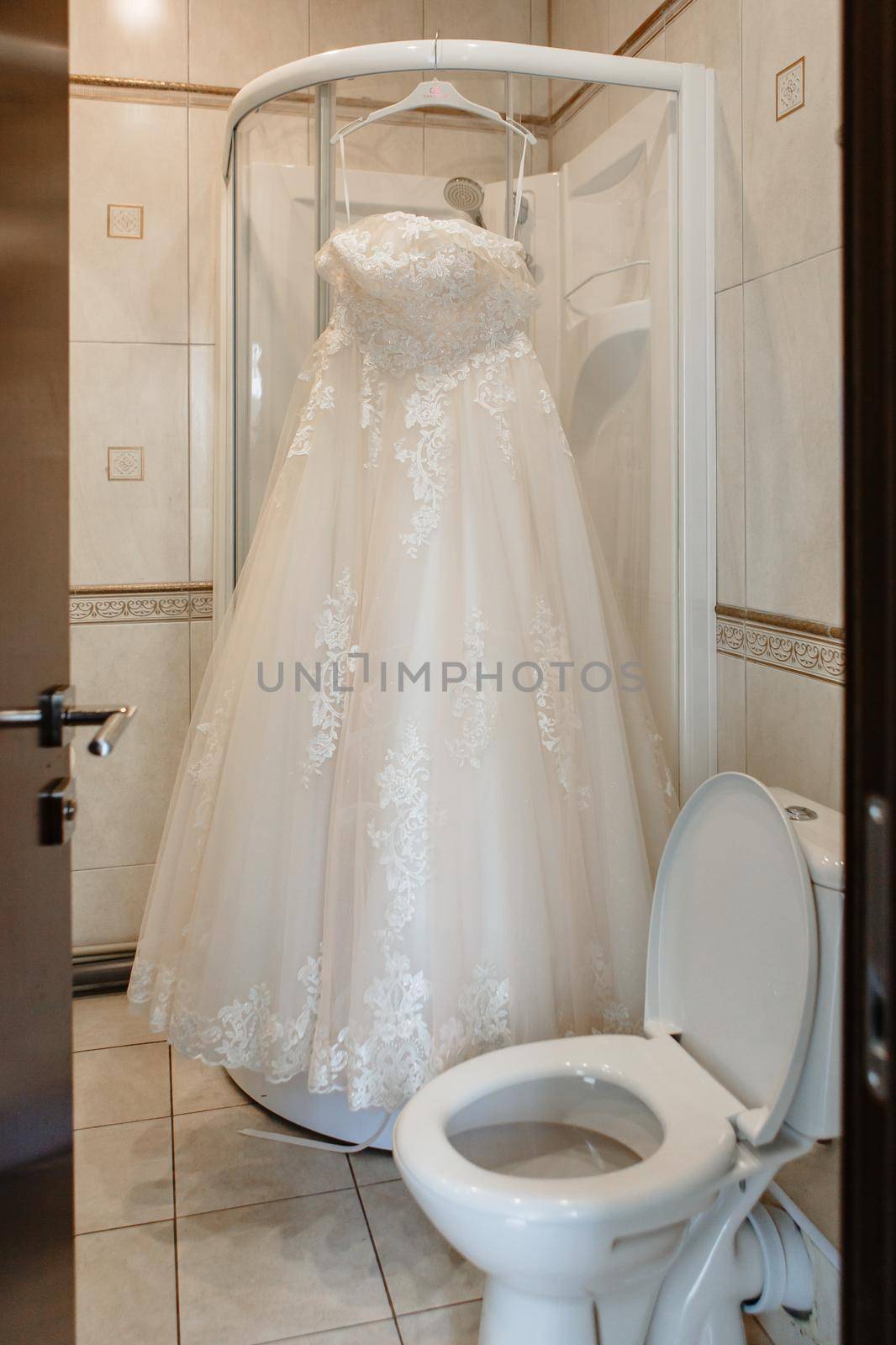 Wedding dress hanging on the shower stall in the bathroom.