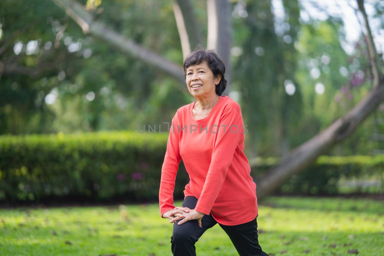 Senior asian woman body warming before exercising. Old woman stretching before jogging in garden, Sport athlete running concept.