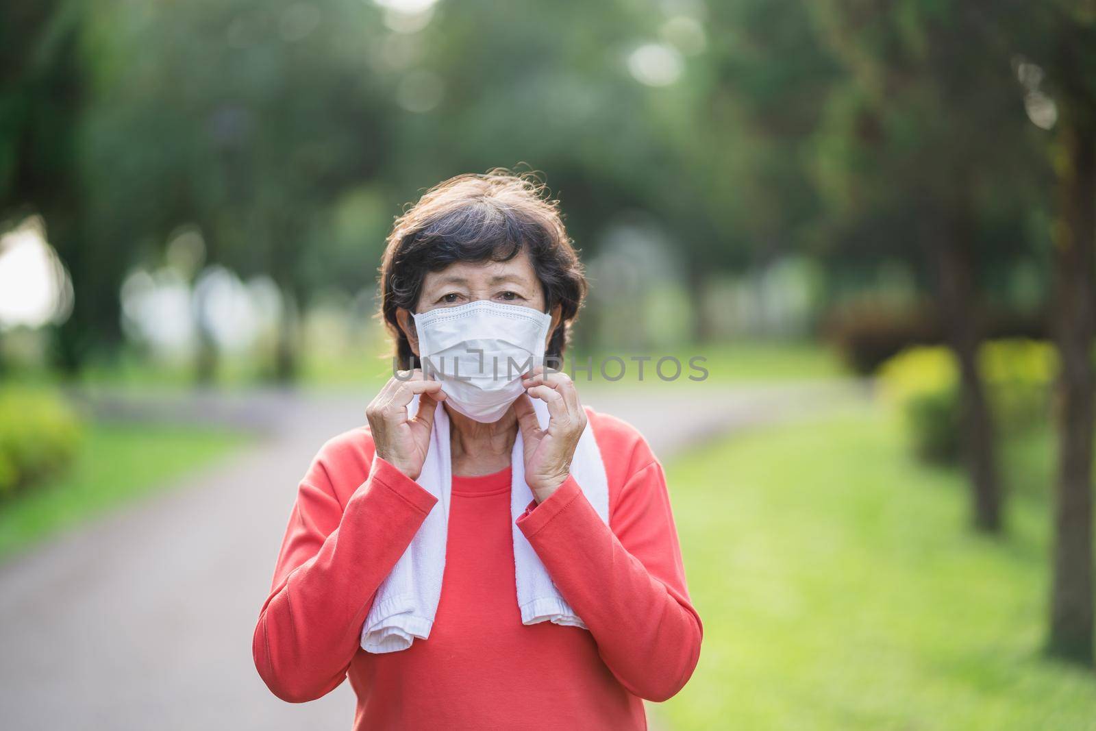 Athletic asian senior woman 60s wearing surgical mask and jogging. Beautiful senior asian woman running at the park on a sunny day. by Wmpix