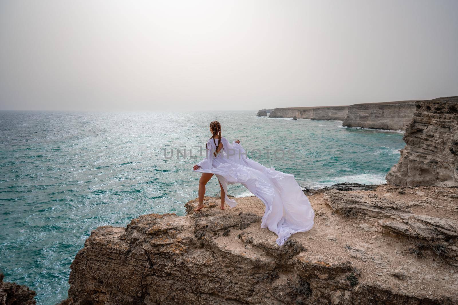 Happy freedom woman on the beach enjoying and posing in white dress over the sea. View of a girl in a fluttering white dress in the wind. Holidays, holidays at sea. by Matiunina