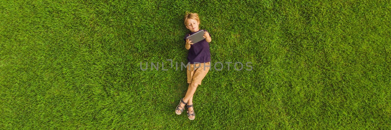 Boy lying on the grass in the park and looks at the tablet. Photos from the drone, quadracopter BANNER, LONG FORMAT by galitskaya