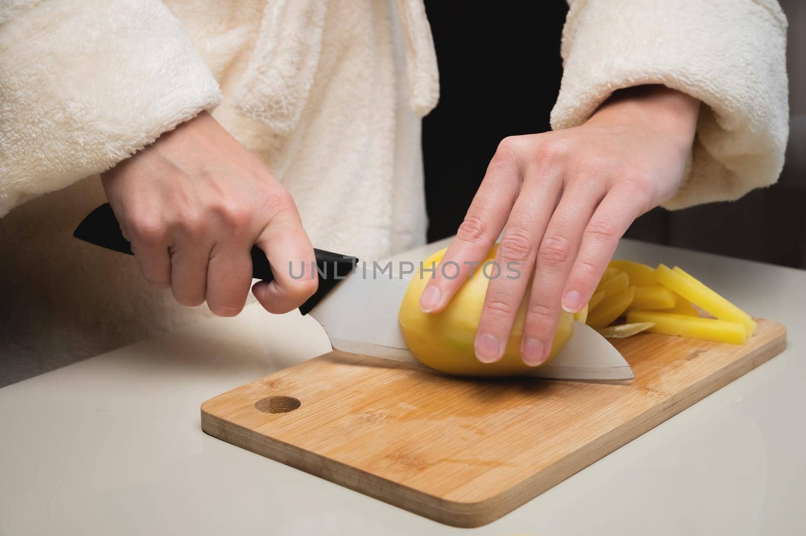 Close-up of female hands cutting peeled potatoes on a wooden cutting board. Home cooking potatoes.