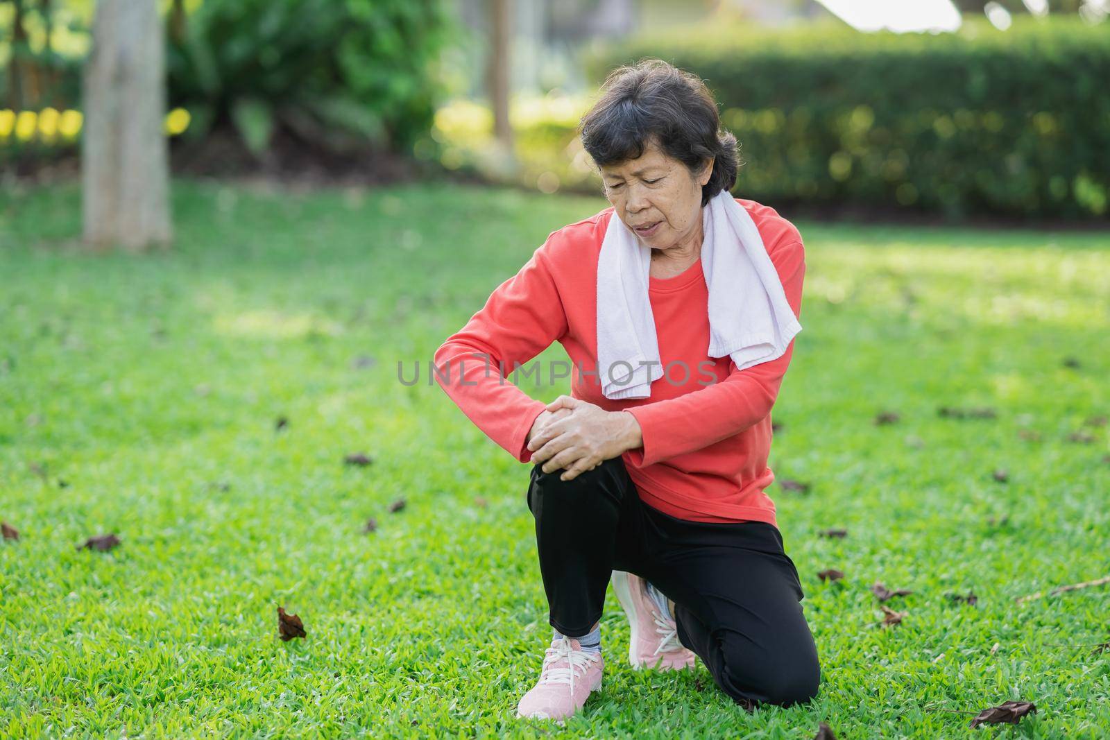 Senior asian woman with knee ankle pain while running in park. Senior asian woman sitting on the ground and holding painful knee.