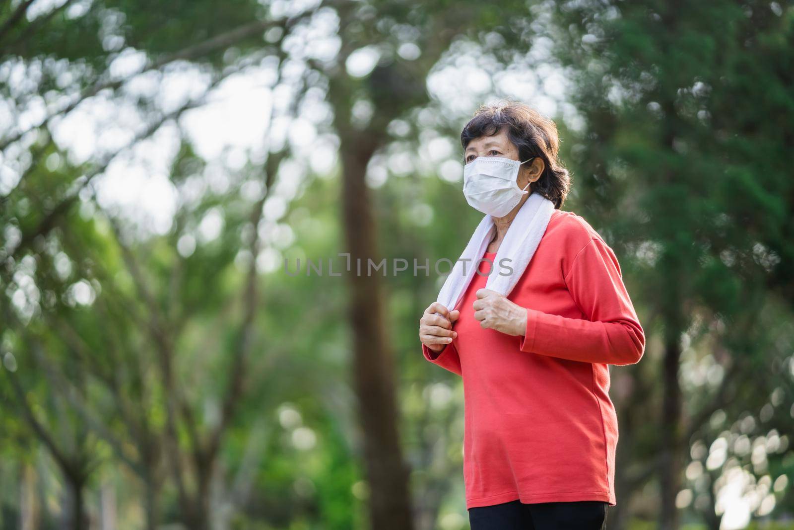 Athletic asian senior woman 60s wearing surgical mask and jogging. Beautiful senior asian woman running at the park on a sunny day. by Wmpix