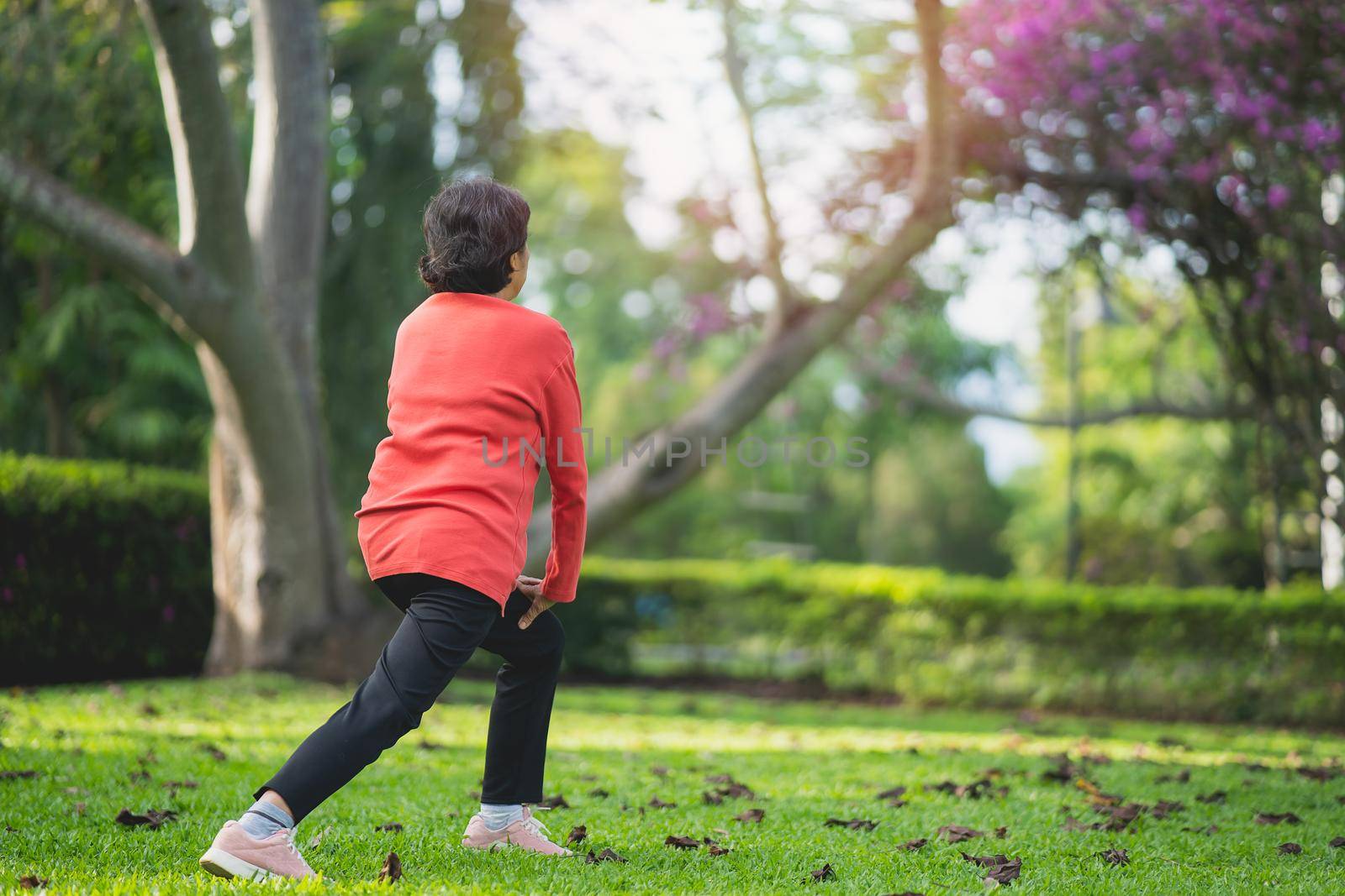 Senior asian woman body warming before exercising. Old woman stretching before jogging in garden, Sport athlete running concept.