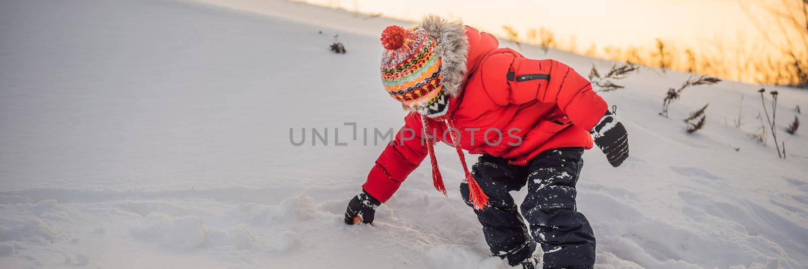 Boy in red fashion clothes playing outdoors. Active leisure with children in winter on cold days. Boy having fun with first snow. Happy little kid is playing in snow, good winter weather BANNER, LONG FORMAT by galitskaya