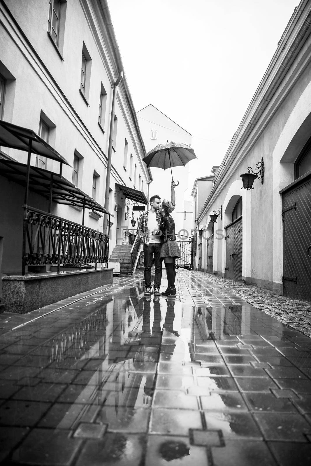 happy, loving couple kissing under an umbrella on a city street on a rainy day by SmartPhotoLab