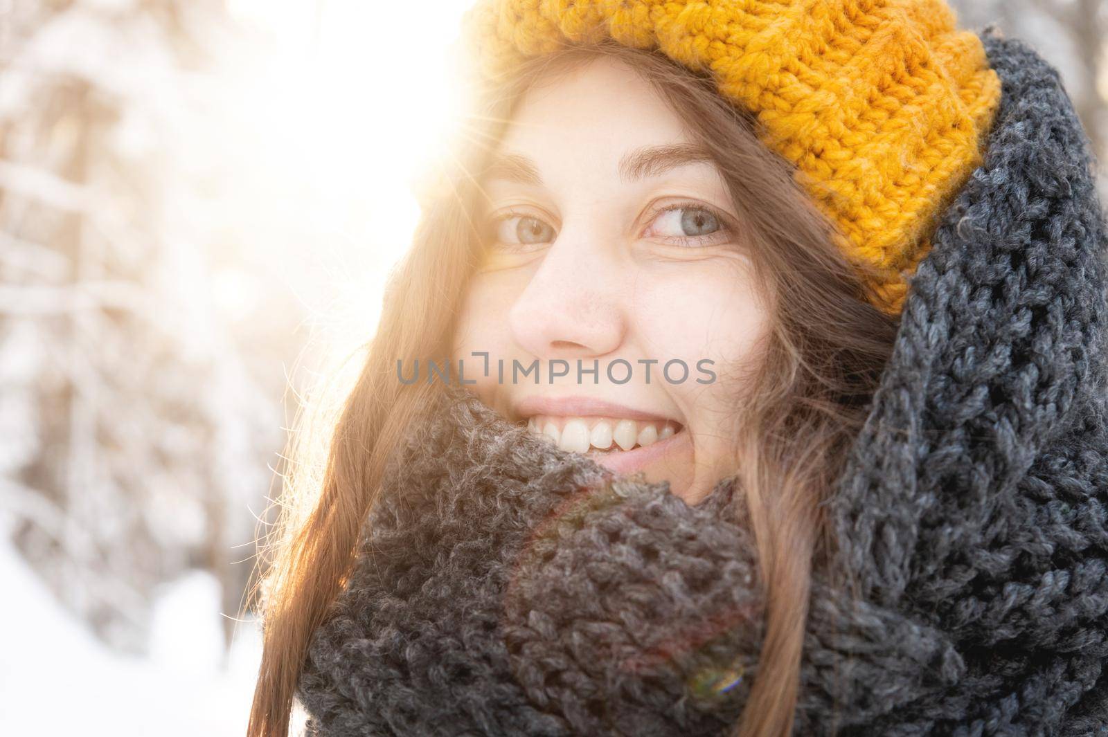 portrait of a smiling young caucasian woman in a bright woolen hat and scarf, against the backdrop of a snowy forest. by yanik88