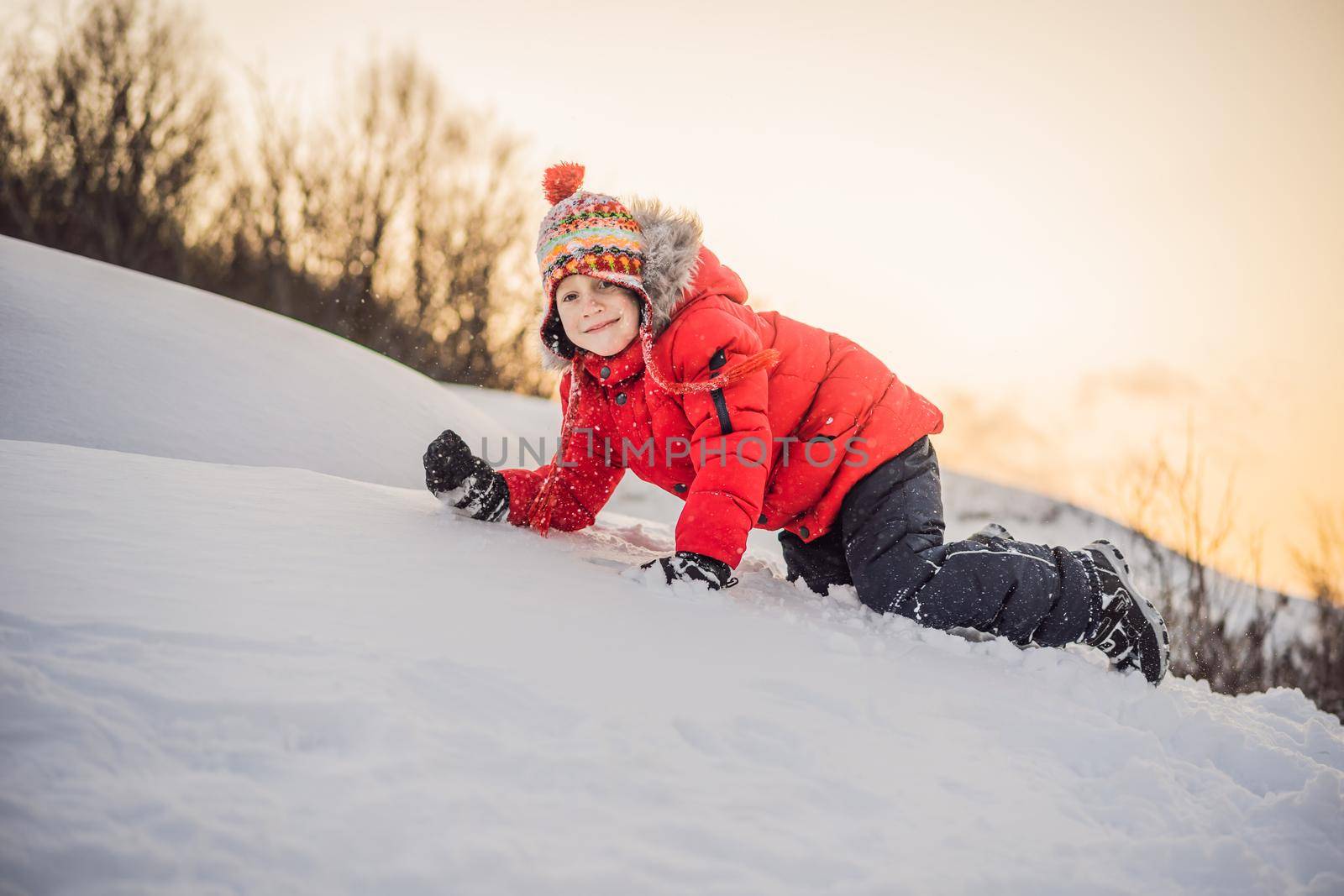Boy in red fashion clothes playing outdoors. Active leisure with children in winter on cold days. Boy having fun with first snow. Happy little kid is playing in snow, good winter weather.