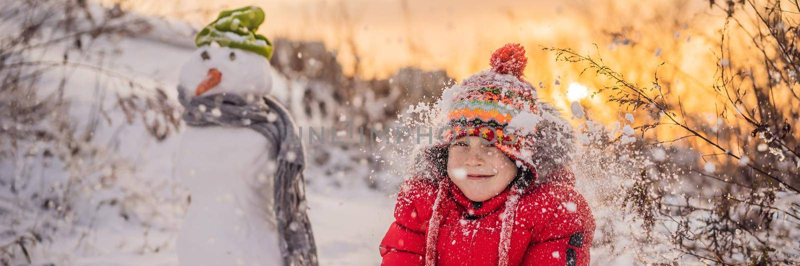 Cute boy in red winter clothes builds a snowman. Winter Fun Outdoor Concept BANNER, LONG FORMAT by galitskaya