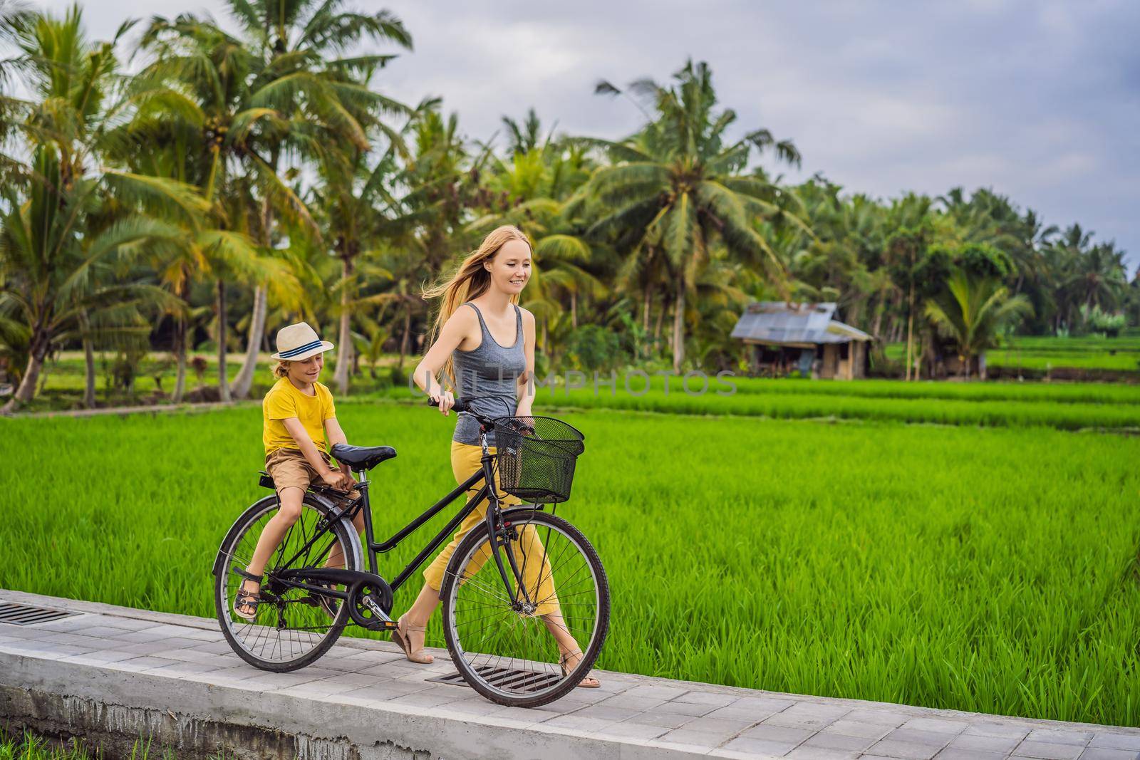 Mother and son ride a bicycle on a rice field in Ubud, Bali. Travel to Bali with kids concept by galitskaya