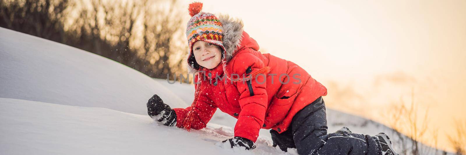 Boy in red fashion clothes playing outdoors. Active leisure with children in winter on cold days. Boy having fun with first snow. Happy little kid is playing in snow, good winter weather BANNER, LONG FORMAT by galitskaya