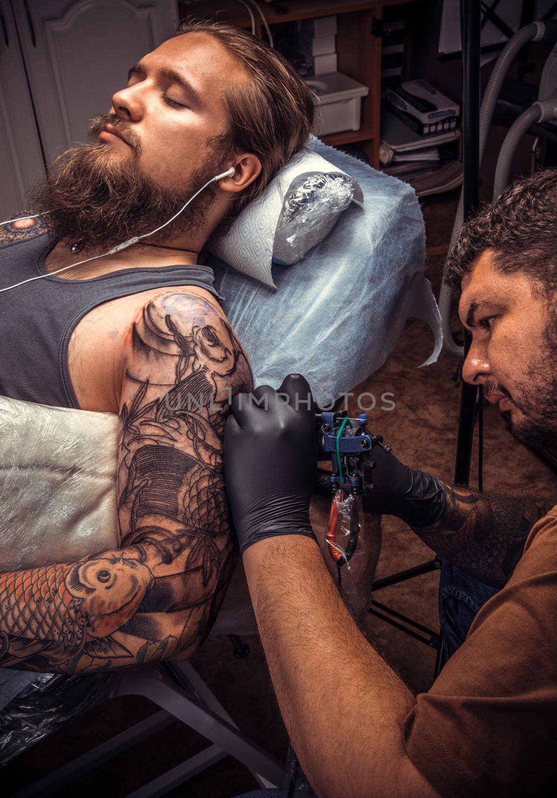 Tattooer doing tattoo in tattoo parlour./Professional tattooist working tattooing in salon.