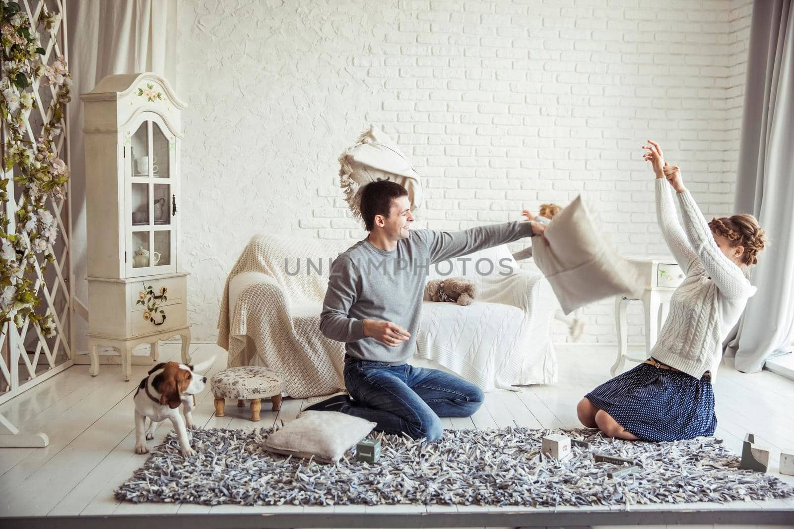 happy husband and wife jokingly holds a pillow fight on the sofa in the living room