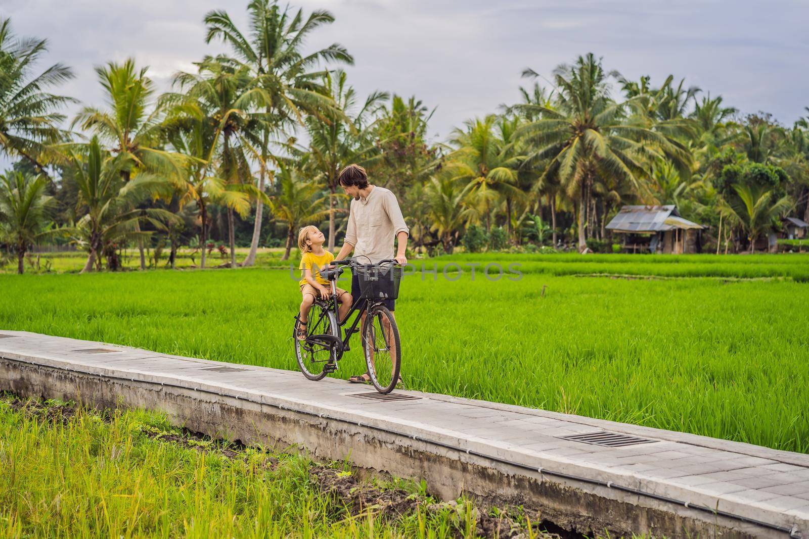 Father and son ride a bicycle on a rice field in Ubud, Bali. Travel to Bali with kids concept by galitskaya