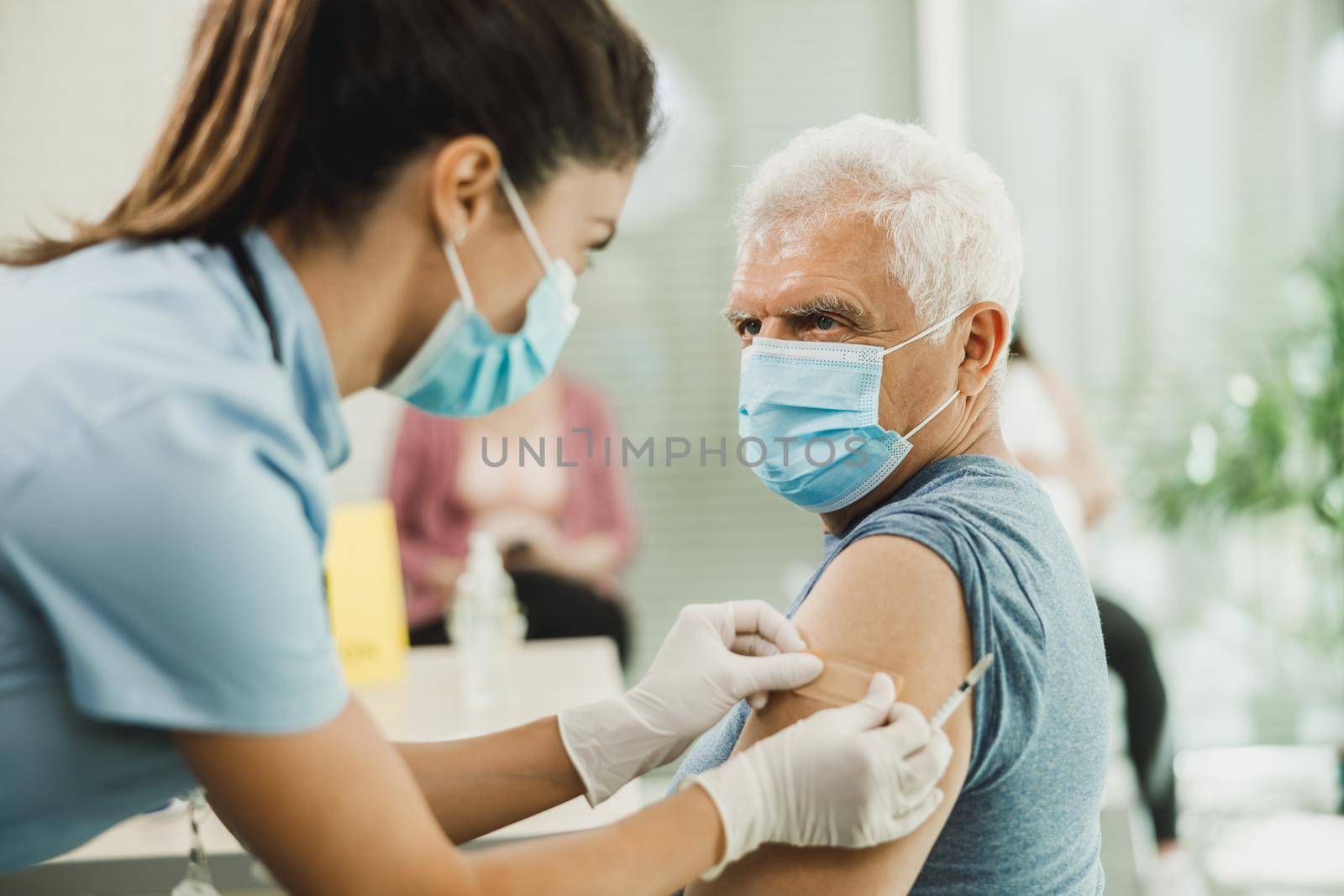 A nurse applying a band aid to a senior man after receiving a vaccine due to coronavirus epidemic.