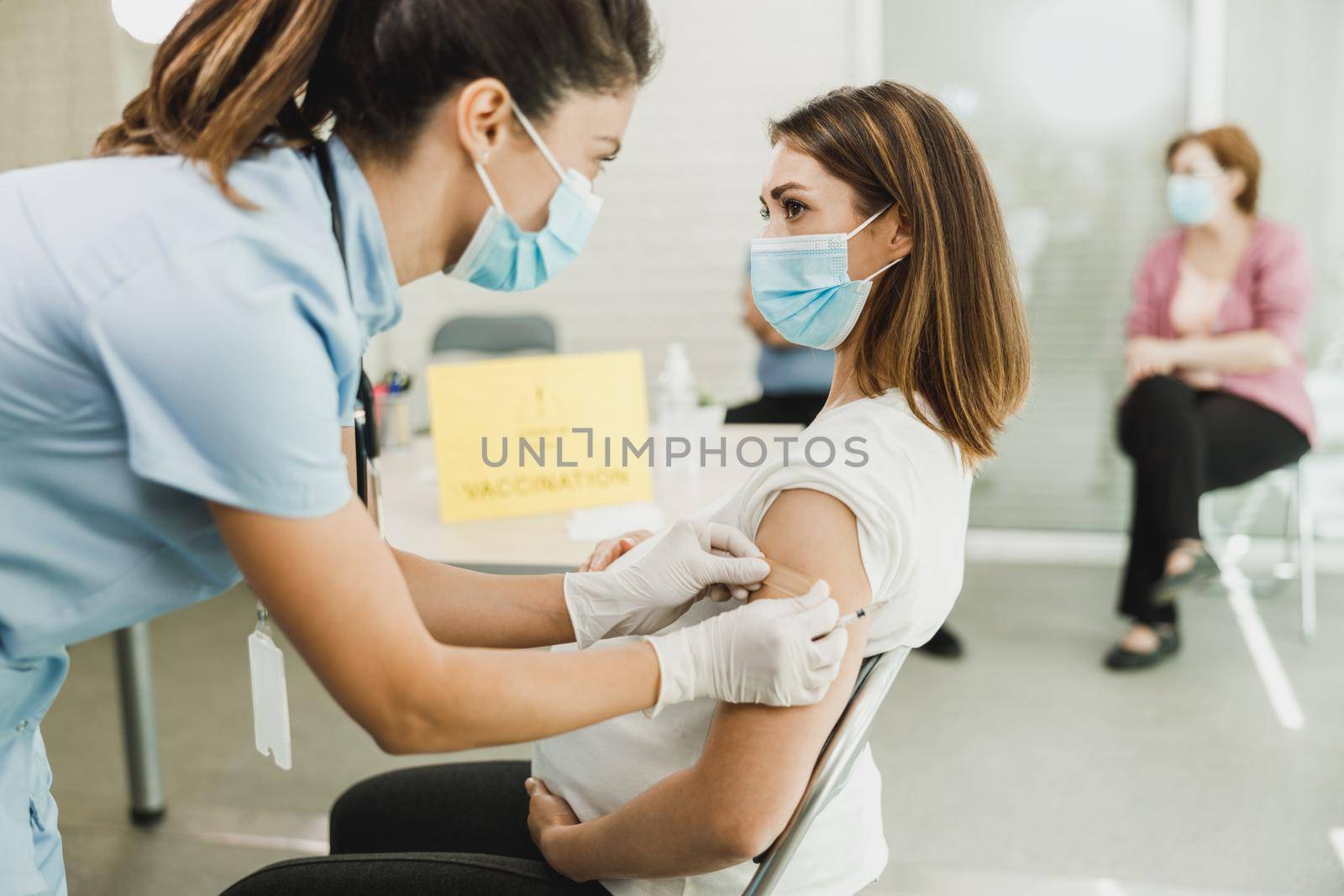 A nurse applying a band aid to a young pregnant woman after receiving a vaccine due to coronavirus epidemic.