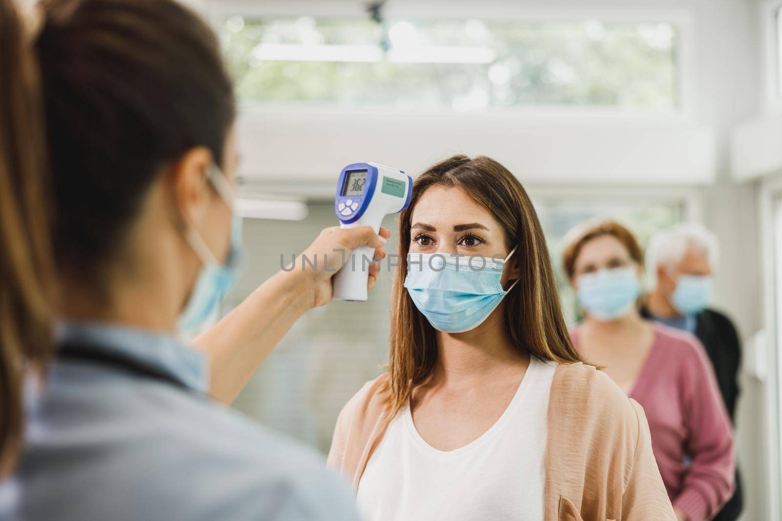 Nurse measuring temperature of a young woman while waiting in a row before vaccination against coronavirus.