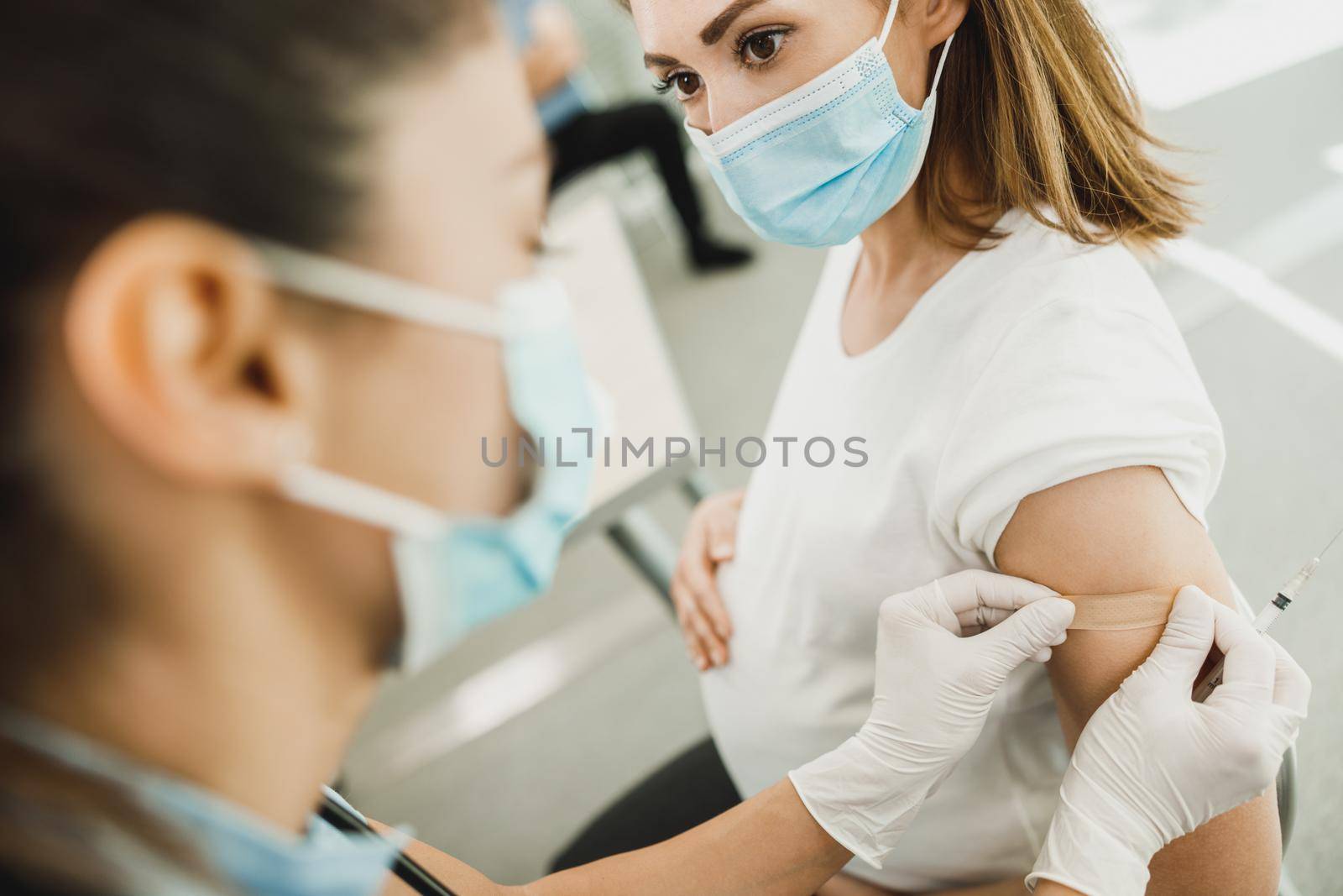 Close-up of a nurse applying a band aid to a young pregnant woman after receiving a vaccine due to coronavirus epidemic.
