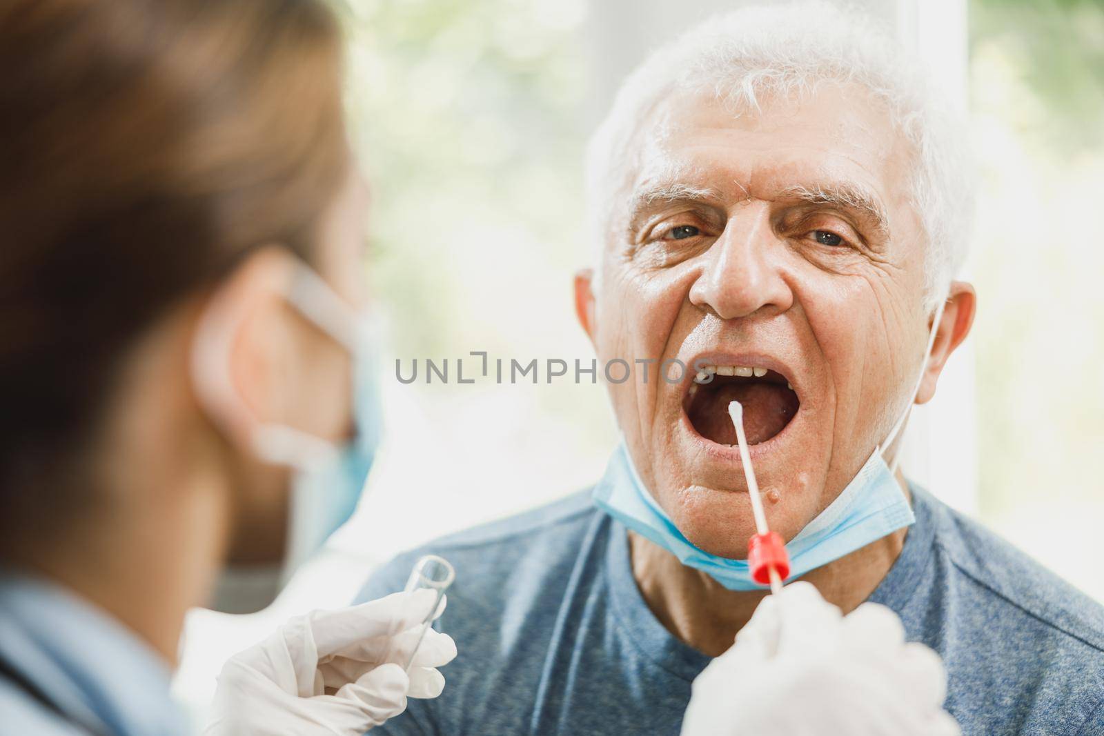 A senior man having swab medical test from throat during coronavirus pandemic.