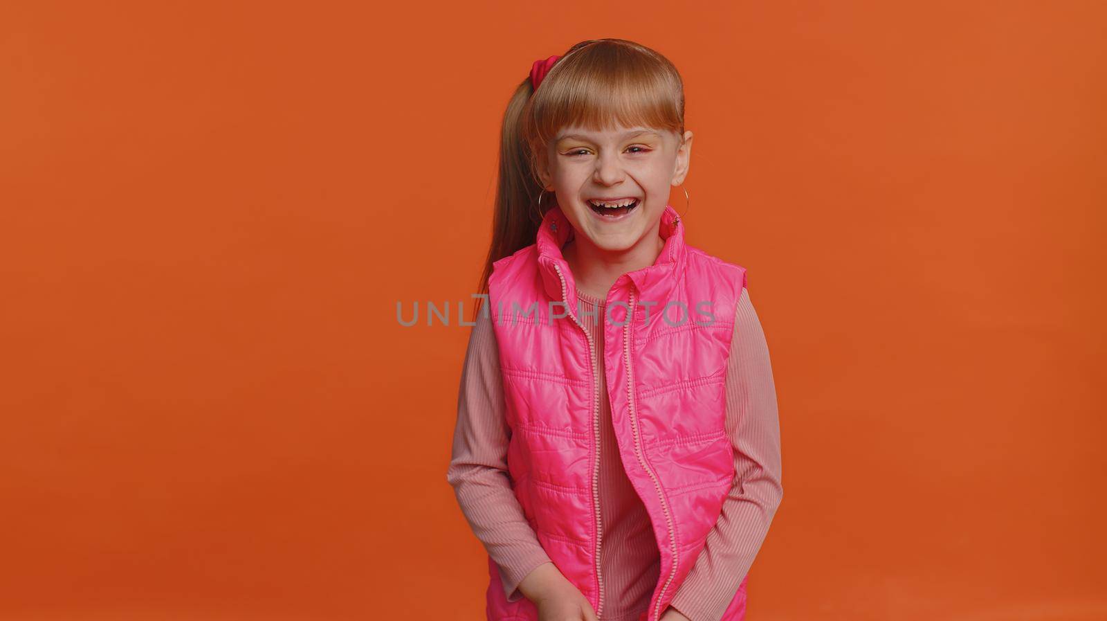 Joyful girl laughing out loud after hearing ridiculous anecdote, funny joke, feeling carefree amused, positive people lifestyle. Young little child kid isolated alone on orange studio wall background